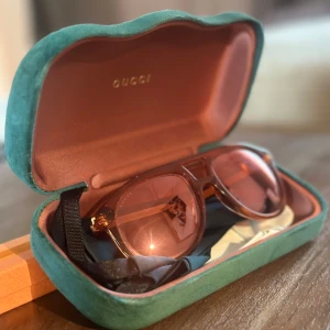 Solglasögon från Gucci (i nyskick) - Säljer ett par snygga Gucci-solglasögon i nyskick med orange tonade glas och transparent orange båge. De kommer i ett lyxigt fodral med mjuk insida. Perfekta för att ge din outfit en touch av stil och elegans. Använd dem för att skydda dina ögon med klass!