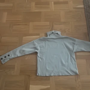 Grå polotröja med knappar - Stilren och mysig gråa polotröja med långa ärmar. Tröjan har tre snygga knappar på ärmsluten som är så söt! Perfekt för kyliga dagar och passar till både vardag och lite finare tillfällen. Superbekväm och lätt att matcha med andra plagg🍂