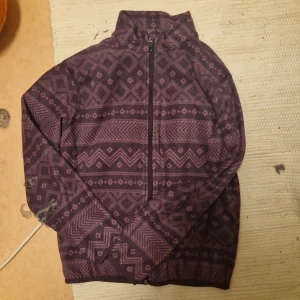 Mönstrad fleecejacka från Everest - Säljer en mysig fleecejacka från Everest i storlek 146/152. Den är lila med ett coolt geometriskt mönster och har en dragkedja framtill. Perfekt för kyliga höst- och vinterdagar. Håll dig varm och stilren! 💜