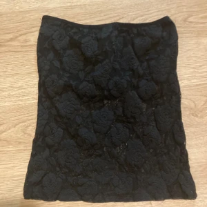 Svart tubtopp i spets blommönster  - Svart tuptopp i spets med blomönster, hela toppen är genomskinlig förutom ett svart band framtill över bysten  Ingen lapp men upskattat storlek s-xs