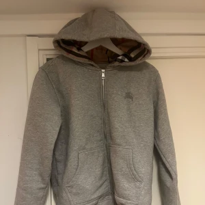 Grå burberry hoodie - Säljer en snygg grå burberry hoodie i bomull. Perfekt för höst och vår, med en stilren look som funkar till det mesta, Tröjan är i mycket bra skick och redo för nya äventyr!