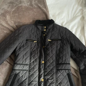 Svart quiltad jacka från Stockh LM - Säljer en snygg svart quiltad jacka från Stockh LM i storlek L. Jackan har en stilren design med guldknappar och dragkedjor. Den är perfekt för höst och vår, med en bekväm passform och hög krage i manchester. Perfekt för dig som vill ha en stilren look! 🖤