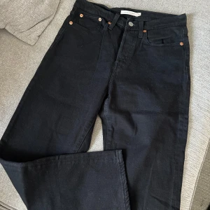 Svarta jeansbyxor Levi’s - Säljer ett par klassiska svarta jeansbyxor i mycket bra skick. De har en högmidjad passform och raka ben, perfekt för både vardag och fest. Byxorna har knappar och en dragkedja framtill. Ett måste i garderoben för alla som älskar stilrena plagg!