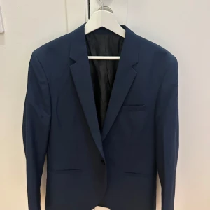 Blå kavaj från H&M - Säljer en stilren blå kavaj från H&M i skinny fit. Perfekt för både fest och formella tillfällen. Kavajen har en klassisk design med knappar framtill och är i mycket bra skick. Passar utmärkt till vår och sommar.