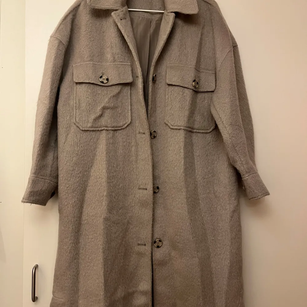 Säljer en snygg beige kappa från Gina Tricot i storlek S, oversize. Den har en klassisk design med knappar framtill och stora fickor på bröstet. Perfekt för höst, vår och vinter, och ger en stilren look till vilken outfit som helst. Passar både till vardags och lite finare tillfällen. Sparsamt använd!. Jackor.