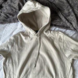 Beige hoodie från BOSS - Säljer en snygg beige hoodie från BOSS i storlek M. Den är i mycket bra skick och har en klassisk design med dragsko i huvan. Perfekt för höst och vår, och den är supermjuk och bekväm. Passar både till vardags och chillkvällar. 🧥✨
