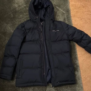 Svart dunjacka från Cross Sportswear - Säljer en svart dunjacka från Cross Sportswear i storlek XS. Jackan är perfekt för kalla dagar med sin varma dunfyllning och har en praktisk huva. Den har dragkedja framtill och är i mycket bra skick. Perfekt för vintern! ❄️