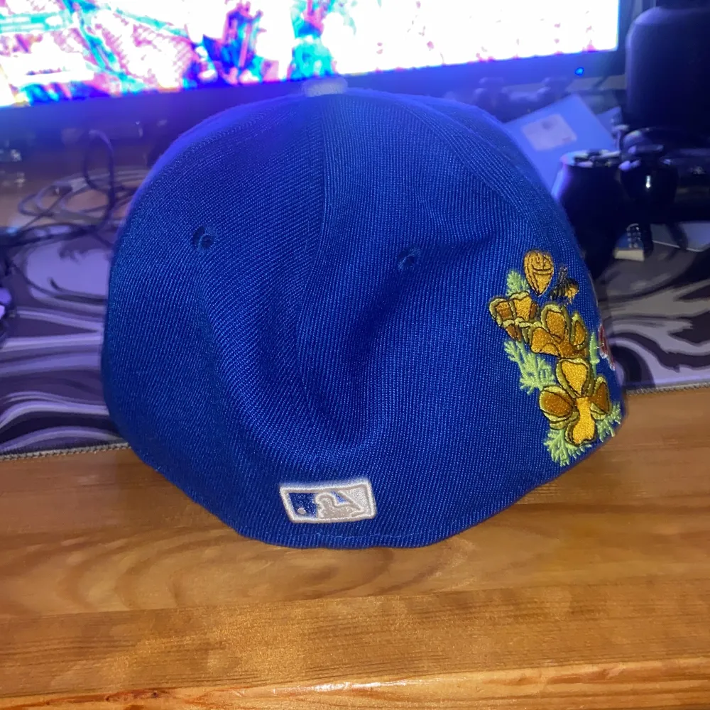 Säljer en blå New Era 59FIFTY keps med LA-logga framtill och blommigt broderi på baksidan. Kepsen är i bra skick och har en platt skärm. Perfekt för sommarens alla äventyr eller som en cool accessoar till vardagsoutfiten.. Accessoarer.