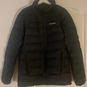 Svart pufferjacka från Columbia - Säljer en svart pufferjacka från Columbia i storlek L. Jackan är perfekt för kalla dagar med sitt quiltade mönster och långa ärmar. Den har en dragkedja framtill och är i mycket bra skick. Insidan har ett reflekterande foder för extra värme. Perfekt för vinter och höst! Finns att hämta i Lund. Kan skickas, köpare står för frakt.