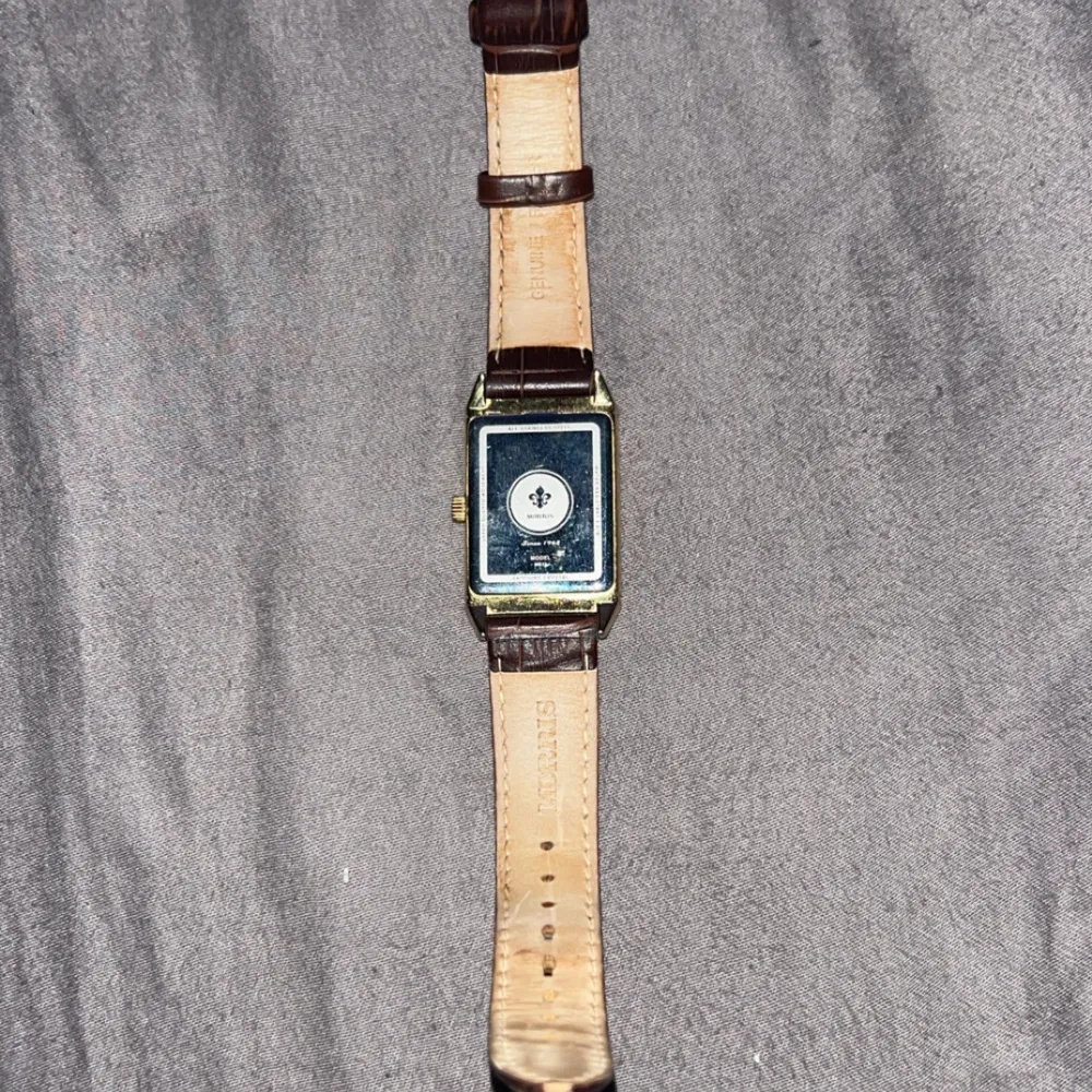 Säljer en stilren herrklocka från Morris med rektangulär urtavla i guld och vit bakgrund. Klockan har ett brunt läderarmband med krokodilpräglat mönster. Perfekt för både vardag och fest. Klockan är i bra skick och har en klassisk design som aldrig går ur tiden. Pris kan diskuteras.. Asusteet.