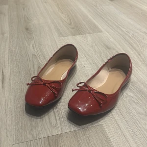 Röda ballerinaskor med rosett - Säljer ett par snygga röda ballerinaskor i glansigt material. De har en söt rosett framtill och är perfekta för både vardag och fest. Skorna är i mycket bra skick och passar perfekt till en somrig outfit eller en färgglad höstlook.