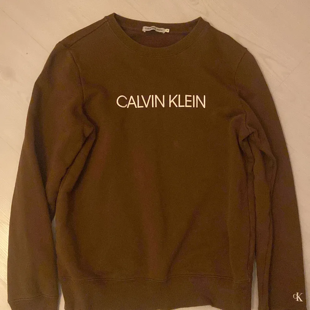 Säljer en snygg brun tröja från Calvin Klein med deras ikoniska logga på bröstet. Tröjan är i ett mjukt material och har långa ärmar. Perfekt för en avslappnad stil eller att bära till vardags. Passar bra till både jeans och chinos. Har en liten ljus fläck. Men den är inte så synlig.. Tröjor & Koftor.