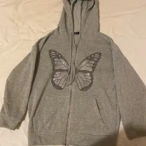 Säljer en supermjuk och bekväm grå hoodie från Shein med en snygg fjärilsdesign på framsidan. Perfekt för mysiga dagar eller en avslappnad stil. Den har dragkedja och en stor huva för extra komfort. Passar perfekt till jeans eller leggings!