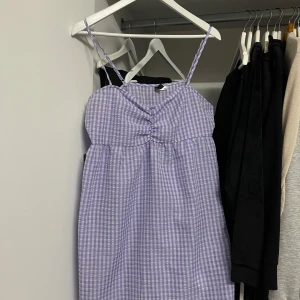 Lila rutig klänning från H&M - Säljer en superfin lila rutig klänning från H&M. Den har smala axelband och en söt rynkdetalj framtill. Perfekt för sommardagar eller en avslappnad fest. Klänningen har en dragkedja på sidan för enkel påklädning. Storlek 40, passar M. Aldrig använd 