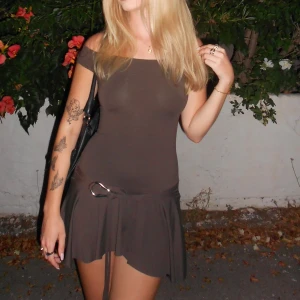 Grön/brun Minidress - Säljer en superfin brun/grön kortklänning med en söt volangdetalj längst ner. Klänningen har en offshoulder-design men går att ha över axlar också. Endast använd 1 gång!!