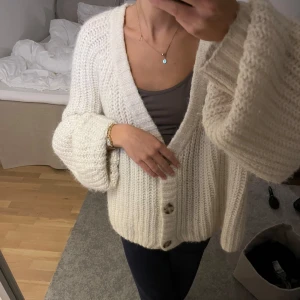 Vit stickad kofta - Mysig och varm vit stickad kofta med stora knappar framtill. Perfekt för kyliga dagar och ger en avslappnad look. Koftan har långa ärmar och en lös passform som gör den superbekväm att bära. Alpacka tyg.