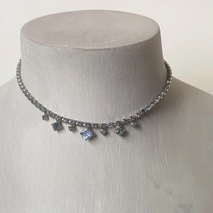 Glittrigt halsband med blå stenar - Säljer ett supervackert glittrigt halsband med blå stenar. Halsbandet har en rad av små gnistrande stenar och större fyrkantiga blå stenar som hänger ned. Perfekt för att ge lite extra bling till din outfit! 💎