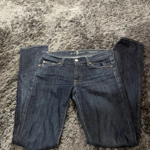 Mörkblå jeans från 7 for All Mankind - Säljer ett par snygga mörkblå jeans från 7 for All Mankind. De har en klassisk femficksdesign med knappar och dragkedja framtill. Jeansen är i en straight passform och är tillverkade av bomull med en liten del elastan för extra komfort. Perfekta för både vardag och fest!