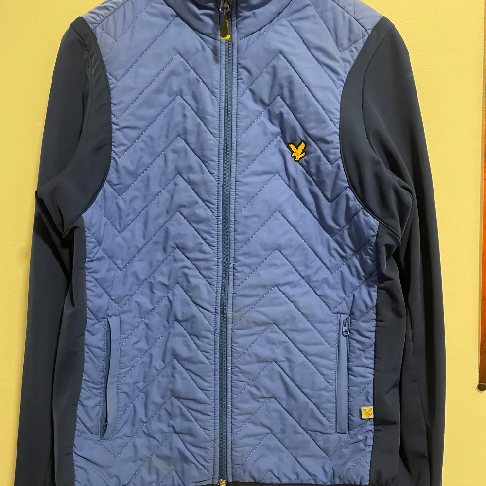 Säljer en snygg blå quiltad jacka från Lyle & Scott. Jackan har en dragkedja framtill och ett coolt mönster. Den är perfekt för höst och vår med sina långa ärmar och bekväma passform. Detaljer som den gula loggan på bröstet ger den en extra touch. Perfekt för både vardag och fest!. Jackor.