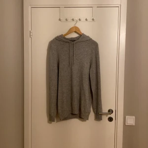 Grå stickad hoodie från Dressmann - Säljer en supermysig grå stickad hoodie från Dressmann. Perfekt för kyliga dagar med sin mjuka och varma känsla. Den har en klassisk passform med långa ärmar och en praktisk huva med snörning. Perfekt för både vardag och avslappnade tillfällen!