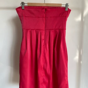 Cerise bamdeauklänning i stl 38. - Väldigt bra skick då jag endast använt klänningen 3-4 ggr. Klänningen är axelbandslös, figursydd överdel och lösare passform nertill. Den har även fickor i sidorna. Jag upplever att färgen är mer cerise i verkligheten än vad bilderna visar. Pris inkl. frakt