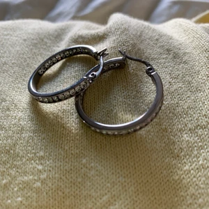 Silvriga örhängen  - Silvriga örhängen ifrån Edblad. Nickelfria. Formade som ringer med ”diamanter” på ena sidan. 