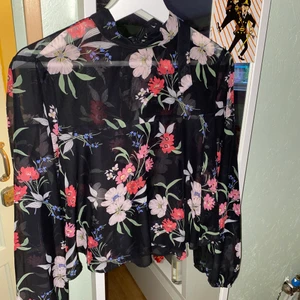 Blommig mesh blus med knytning i nacken  - Blusen är använd 1 gång. Den är långärmad och har något av en liten hög krage, men inget som är störande. Får inte blusen till någon användning. 
