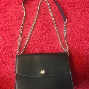 Superfin Tory Burch väska i mycket bra skick  - Säljer väska från Tory Burch i mycket bra skick. Väskan är svart med gulddetaljer. Bandet går att reglera i två längder (se bilder). Vid intresse kan jag självklart skicka fler bilder. 