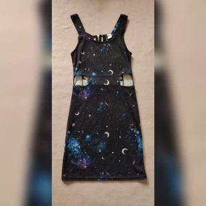 Galaxy-klänning - Figurnära miniklänning med galaxy-motiv i stretchig trikå. Fin ryggdetalj, snygga cutouts i sidorna och även ett väldigt bekväm plagg på grund av stretchen. Den är lite sliten och urblekt i trycket och tyget, se bild. Annars fint skick. Storlek XS.  Finns i Stockholm eller skickas mot frakt.