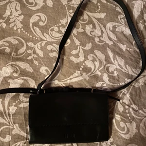 Liten svart väska - Liten svart väska från Kiomi. Har använts sparsamt så den är i fint skick. Väskan har ett fack i mitten som stängs med dragkedja men själva väskan stängs med en knapp. Kan mötas upp i Stockholm eller skicka. Köparen står för frakten 💗