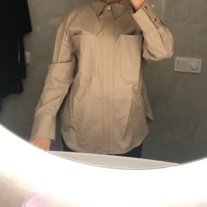 Skjorta från Zara - En supersnygg beige skjorta från zara med dragkedja. Passar storlek 34-38. Har endast använt den 2 gånger 😍 Den är i nyskick ✨