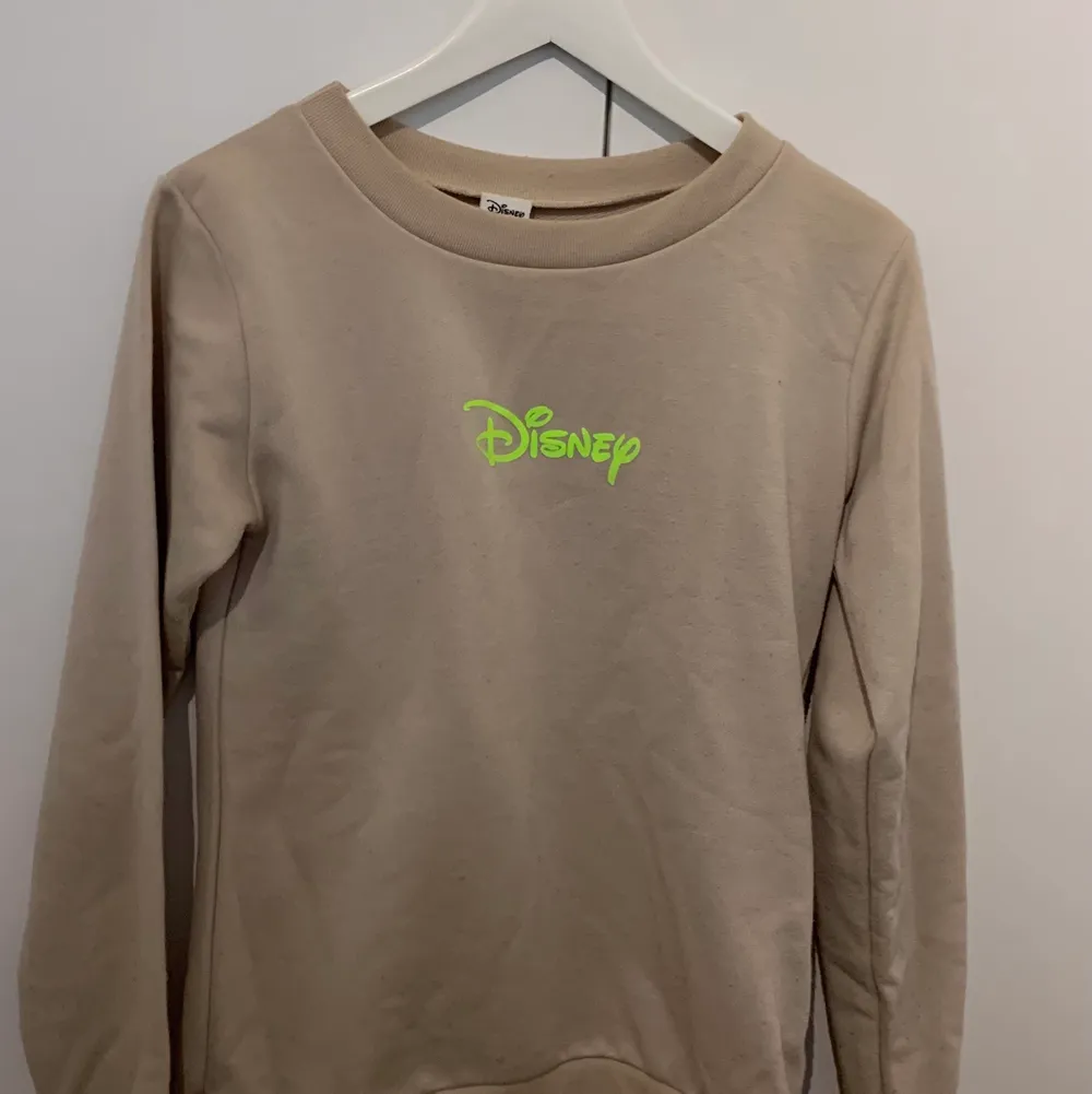 Beige sweatshirt med neon-text. Obs inte från officiella Disney-märket utan är bara ett tryck. Står ingen storlek så jag har uppskattat den till S/M. Frakt 20kr eller gratis vid köp av fler än ett plagg💕. Tröjor & Koftor.