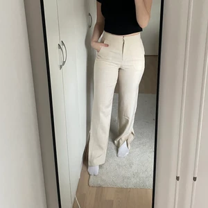 Höga kostymbyxor med slits - Snygga kostymbyxor i ljus-beiget, storlek 36, aldrig använda då dem är för långa för mig, innelängden är 84 cm. Kostymbyxorna är med slits på yttersidan. Från Na-kd:s kollektion med AFJ.