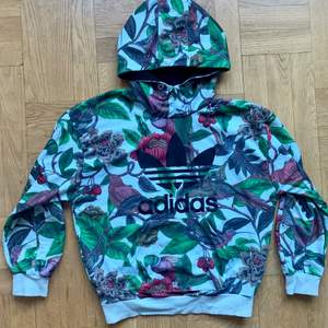 Hoodie från Adidas med blommönster i flera färger. Inga anmärkningar, ser ut som ny. Saknar dock band i luvan. Storlek S, men ganska oversized i modellen så passar nog XS-M beroende på hur man vill att den sitter. 