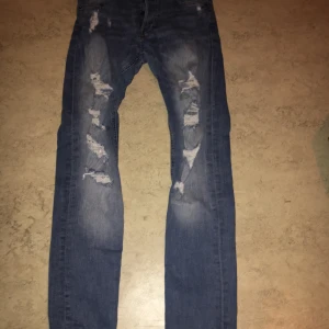 Jeans med slitningar  - Jeans med slitningar på låten och ner mot knät, några även på fickorna, säljes då dom är för små för mig. Köper man fler plagg så kan jag skicka det i samma paket om det önskas 