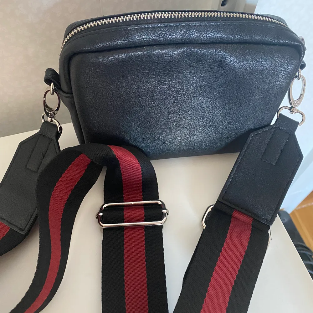 En liten handväska med avtagbar axelrem i svart/rött. Fuskskinn. Endast använd entaka gång.. Väskor.