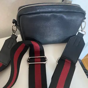 En liten handväska med avtagbar axelrem i svart/rött. Fuskskinn. Endast använd entaka gång.