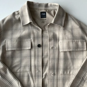 Zara overshirt strl S - Beige overshirt med mörkblått rutmönster från Zara i storlek S. Har använts snålt. En av knapparna har trillat av men knappen har jag sparad och kan skicka med ifall det behövs. Dm för fler bilder :)