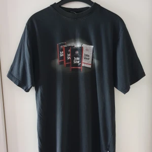 Vintage svart t-shirt - Vintage svart t-shirt med cigarett tryck. Storlek XL, tycker nog den känns mer som ca L/XL. Har några lagningar i sömmarna i armhålorna samt vid lappen i nacken, syns dock inte så mycket (se bild 2). Fraktkostnad blir 50kr. Om många är intresserade kan budgivning bli aktuellt.