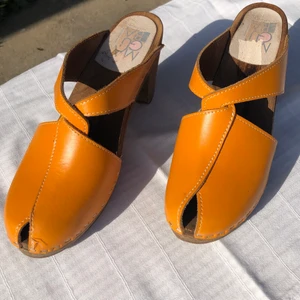 Maguba of Sweden träskor strl 38 - Fina Maguba of Sweden träskor med klack. Skornas färg kommer inte riktigt fram på bilderna men de är mer orangea. Skorna är i strl 38 och är i bra använt skick. Sulan är i trä och ovandelen är i läder. 