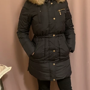 Hollies  - En jätte snygg Hollies jacka i modellen les Arcs,  Svart figursydd dunjacka i en längre modell med avtagbar naturpäls på luvan, stängs med en ordentlig dragkedja fram samt knappar för att hålla kylan borta.