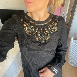 Kort klänning med pärldetaljer, strl S - Svart klänning med snyggt mönster av pärlor, använd varsamt, i bra skick.🧡 Köparen står för frakten