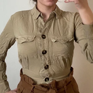 Beige croppad skjorta - Super fin skjorta som jag säljer då den är för liten för mig nu. Den är använd typ 3 gånger. Lättviktig och skönt material som passar super bra nu till sommaren. Spårbar frakt 66kr 🚚 