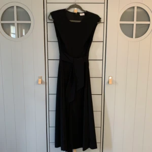 Svart jumpsuit från vila  - Svart jumpsuit från vila. Dragkedja i ryggen, band i midjan för att markera midjan. Super snygg på! Benen är lite kortare så snyggt med en klack eller en snygg sneaker! Jag har även haft stickade tröjor över då jag tycker byxan är super snygg. Nypris: 699kr. Skicka privat för mer bilder! 