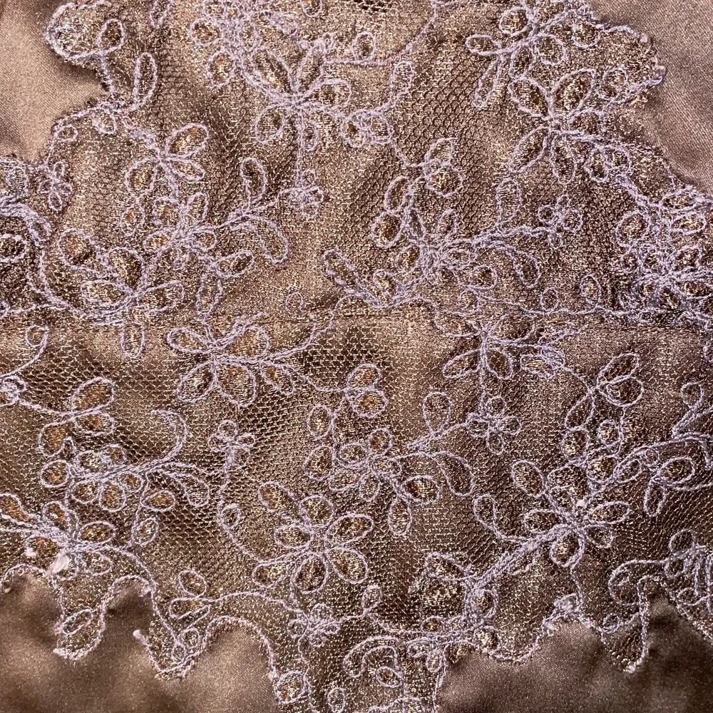 Ett brunt linne/topp i silke med V-ringning med mönster kring V-ringningen och ner. Användes under 2000-talet och väl bevarad. . Toppar.