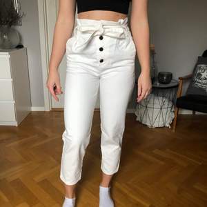 Ett par vita jeans, ankellånga, knappar och knytband i midjan