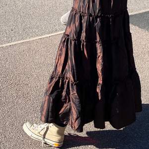 En fin brunglänsande volangliknande kjol. Fint material som lyser i solen. Köpt secondhand men i väldigt bra skick💕 står ingen storlek men är en tjock resor i midjan så passar typ xxs - M/L tror jag.                                                       