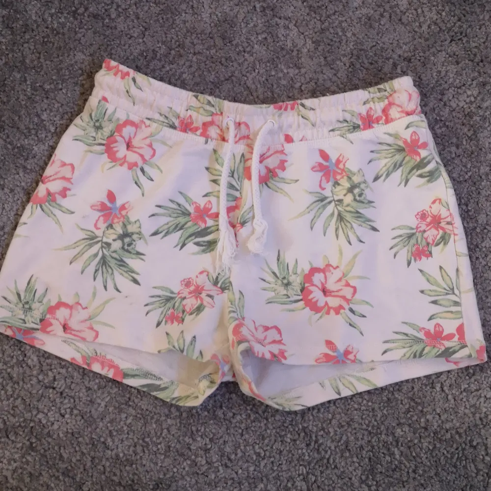 Vita mjukis shorts med rosa exotiska blommor. Är i väldigt fint skick och knappt använda. De har resor i midjan men de går att knyta dem framme. Storlek: 158/164. Inga fickor. . Shorts.