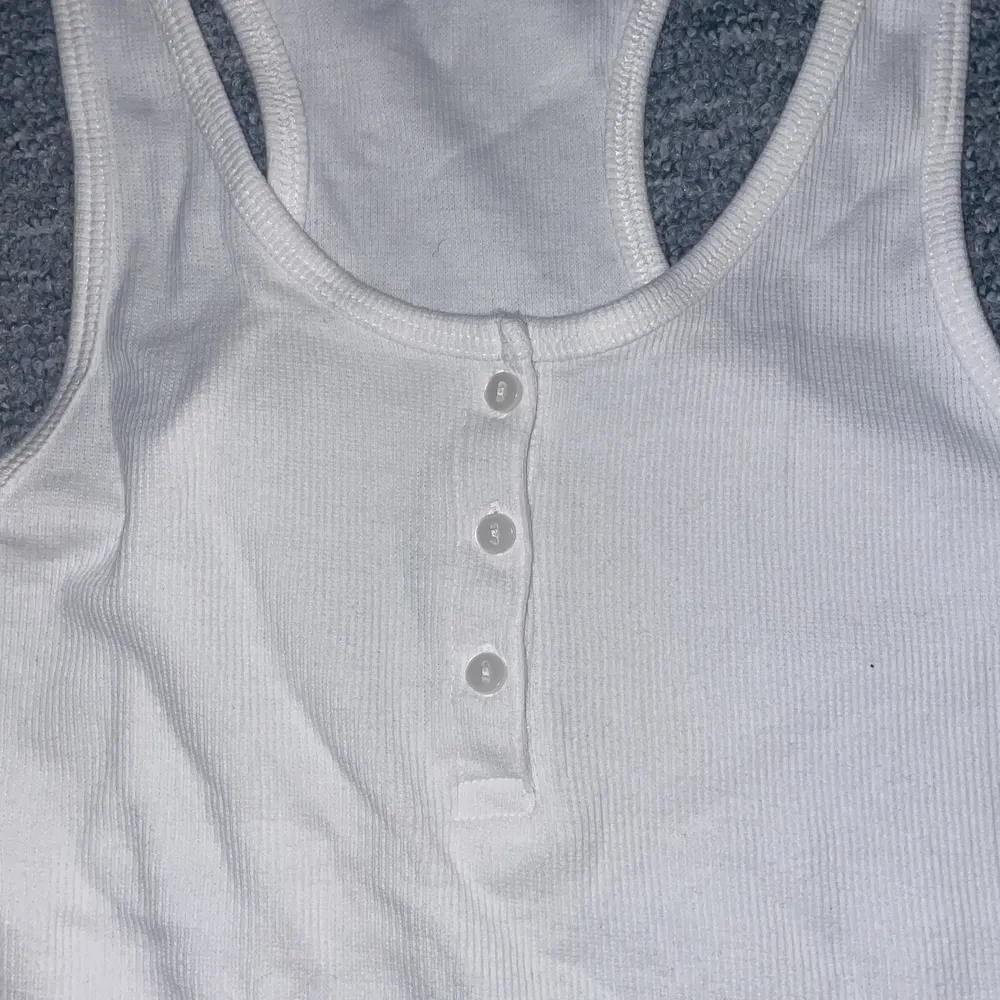 Ett långt vitt linne med vita knappar, ribbat tyg. Storlek S. Kommer inte ihåg när ja köpte de men använder aldrig . Blusar.