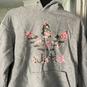 Adidas hoodie - Grå hoodie från adidas med blommigt tryck, använd men i gott skick. Storlek S